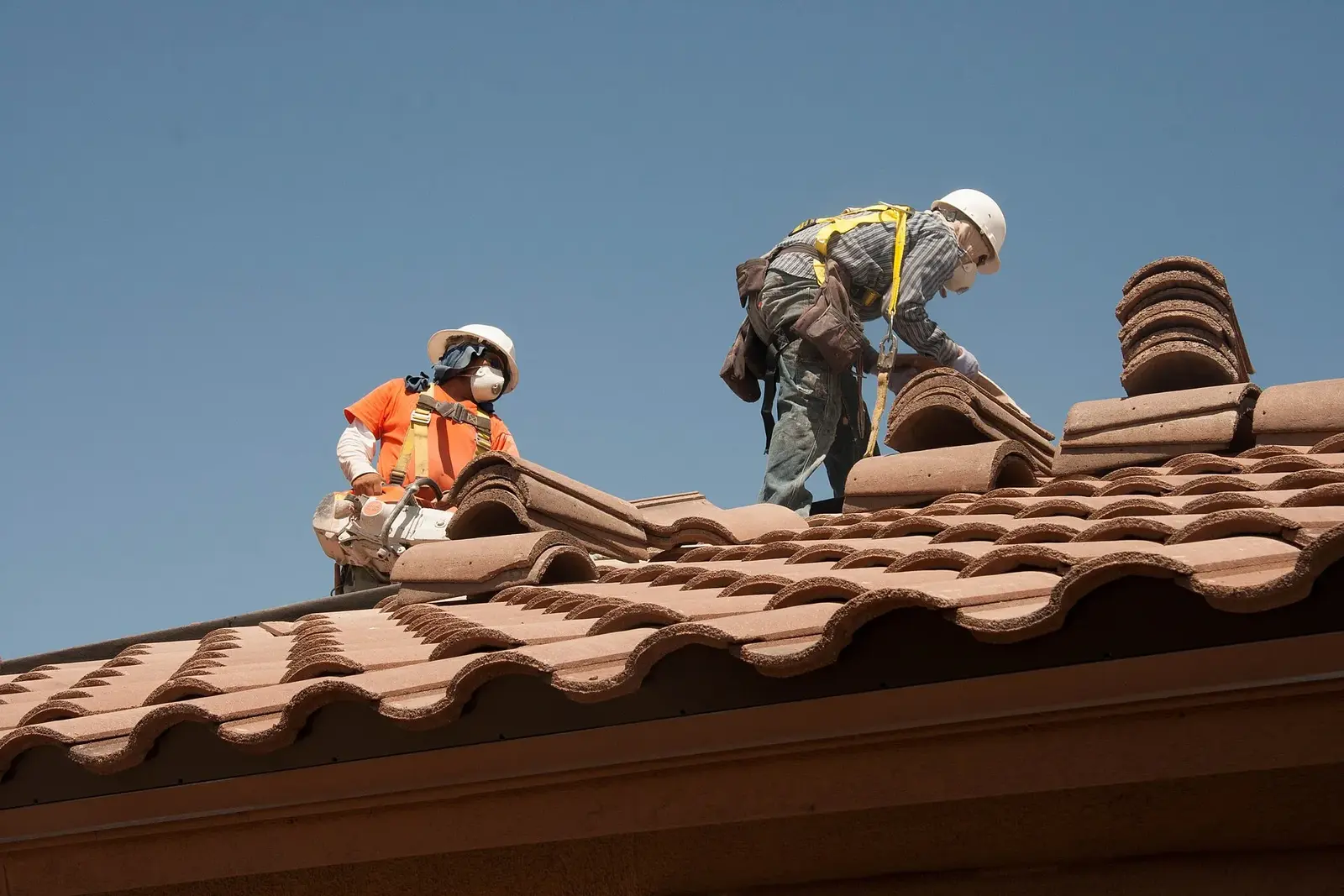 Roofing workers installing tiles on a pitched roof.